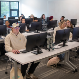 Students engaged in learning at a computer lab. Each has their own computer station and are comfortably spaced.
